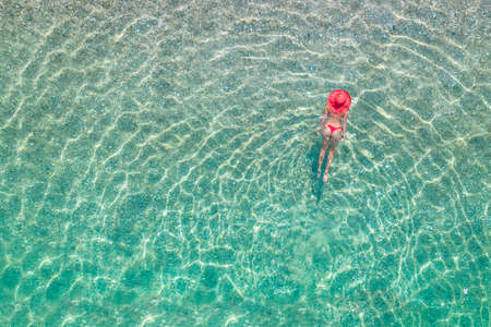 top, aerial view. Athletic body of young beautiful woman in headphones listening music lying and swimming in white bikini in sea water on the sand beach. Drone, copter photo. summer holidays.の写真素材