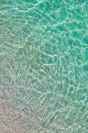 top, aerial view. Young beautiful woman in white bikini swimming in sea water on the sand beach....