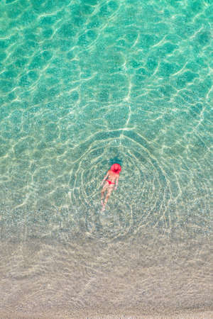 top view. Young beautiful woman in a red hat and bikini swimming in sea water on the sand beach. Drone, copter photo. summer holiday. view from above.の写真素材