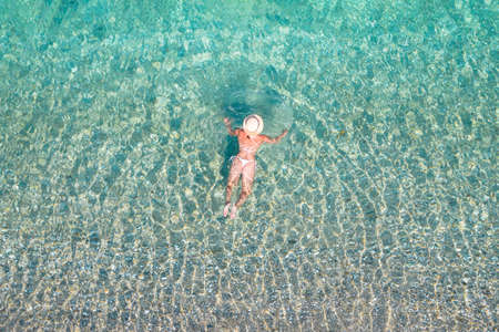 top view. Young beautiful naked woman in a hat swimming in sea water on sand beach. Drone, copter photo. summer holiday. view from above.の写真素材