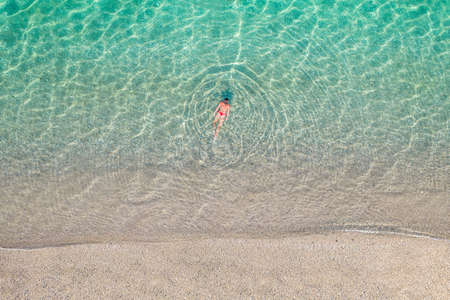 top, aerial view. Young beautiful woman in a hat and white bikini swimming in sea water on the sand beach. Drone, copter photo. summer holidays. view from above.の写真素材