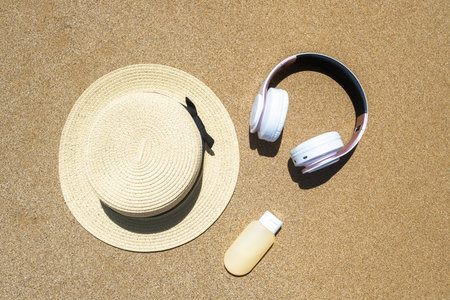 Summer straw hat, headphones and sunscreen lying on the sand of the beach. Travel, holiday, summertime concept. copyspace. top view. flat layの写真素材