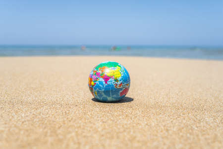Toy globe on the sand of the beach with sea wave background. world travel concept.の写真素材