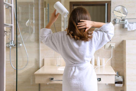 Woman in nightgown applying cream for protective and care dry skin legs sitting on armchair against mirror in bathroom.の写真素材