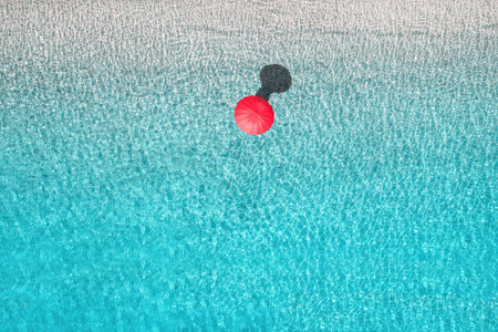 Top view of woman with red summer umbrella walking in tropical blue, turquoise transparent water...