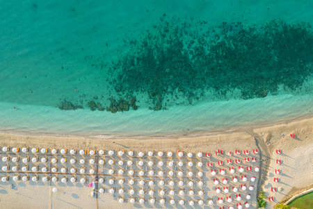 Aerial view of many white sunbed, lounge, umbrellas on sandy beach. Summer and travel concept. Blue, turquoise transparent water surface of ocean, sea, lagoon. Aerial, drone viewの写真素材