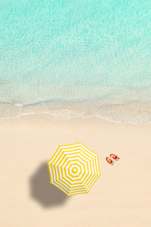 Aerial view of yellow umbrella, flip flops on sandy beach. Summer and travel concept. Blue, turquoise transparent water surface of ocean, sea, lagoon. Aerial, drone view. verticalの写真素材