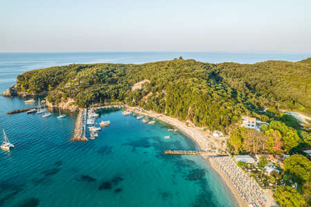 Beautiful colorful houses of seaside town, port of Parga with boats, cruise ship. Sand beach with umbrellas, tourist people, blue, turquoise sea water. Summer holidays and travel concept. Greece. Aerial, drone viewのeditorial素材