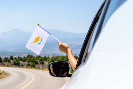 Woman holding Cyprus flag from the open car window driving along the serpentine road in the mountains. Conceptの写真素材