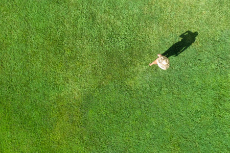 Woman in a white bikini and hat, walking on the green grass sunbathes at summer day. Top view, drone, aerial viewの写真素材