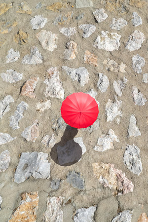 Woman with red rain umbrella walking on the paved stone road protecting herself from the sun at summer day. Top, drone, aerial viewの写真素材