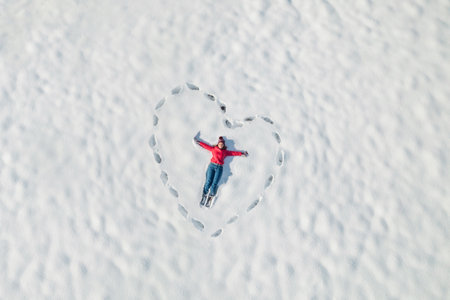 Woman lying on the snow in a heart made from human footprints. Winter. Valentine day, love concept. Drone, top, aerial view.の写真素材