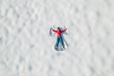 Happy woman lying on the snow at winter, christmas day. Drone, top, aerial view.の写真素材