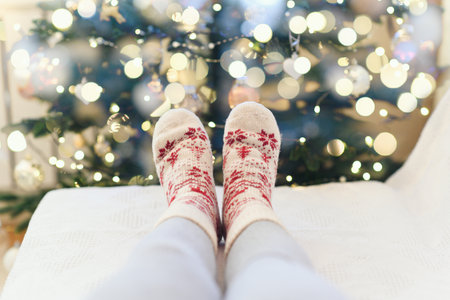 A woman in woolen socks lying on the sofa near Christmas tree with garlandの写真素材
