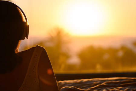 Beautiful woman in nightgown with headphones listening music lying on the bed against sea and palm trees at summer sunny dayの写真素材