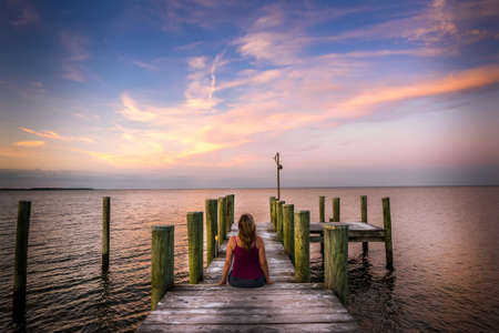 Woman sitting on a pier watching a stunning sunset on the Chesapeake bay in Marylandの写真素材
