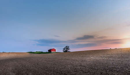 Idyllic farm with red barn in the Maryland countryside with plowed fields at sunset during Springの写真素材