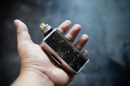 high end black carbon fiber in clear resin regulated box mods with rebuildable dripping atomizer and ultem drip tip in hand on dark grey texture background, vaporizer equipment, selective focusの写真素材