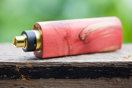 high end red natural stabilized wood box mods with rebuildable dripping atomizer on natural wood texture background, vaporizer equipment, selective focusの写真素材