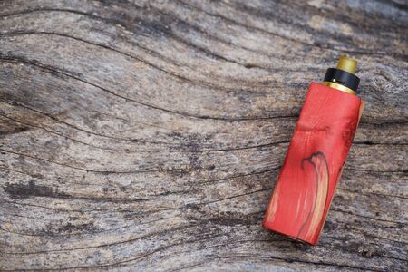 high end red natural stabilized wood regulated box mods with rebuildable dripping atomizer on natural timber wood texture background, vaporizer equipment, selective focusの写真素材