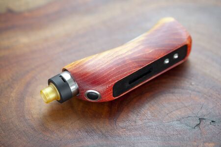 high end red natural stabilized wood box mods with rebuildable dripping atomizer on natural wood texture background, vaporizer equipment, selective focusの写真素材