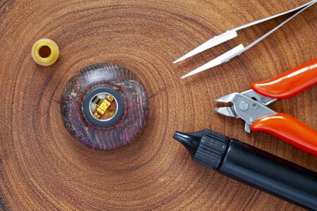 single micro coil with cotton in rebuildable dripping atomizer on stabilized wood atty stand with ultem drip tip, ceramic tweezers, cutting pliers and e juice bottle on natural wood texture backgroundの写真素材