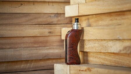 high end rebuildable dripping atomizer with stabilized natural redwood burl regulated box mods on natural wood texture background, vaping device, selective focusの写真素材
