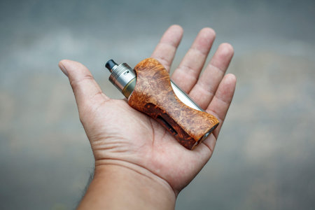 high end titanium genesis atomizer with stabilized natural black ash wood regulated box mods in hand...