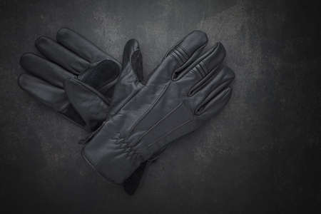 top view shot a pair of new black leather motorcycle gloves classic style for protect biker hands on dark gray, grey, black tone texture background with copy space for textの写真素材