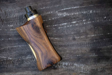 high end rebuildable dripping atomizer with stabilized natural walnut regulated box mods on dark old wood texture background, vaping device, selective focusの写真素材