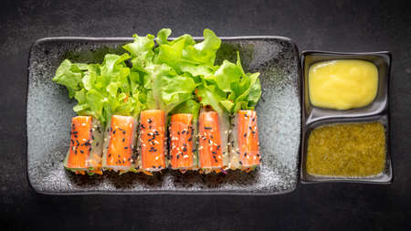 crab stick salad roll with mix organic vegetable, sesame on top and salad dressing in ceramic plate on dark tone texture background, top view, healthy foodの写真素材
