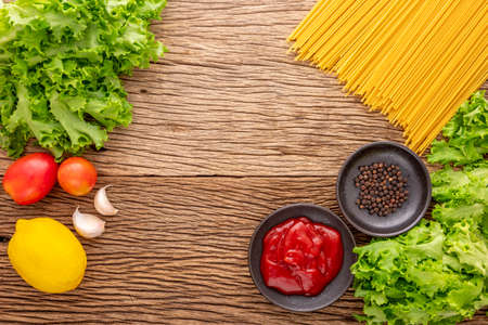 spaghetti pasta with ketchup, pepper, lettuce, tomato, garlic and lemon on rustic natural wood texture background, ingredient for prepare food, top viewの写真素材