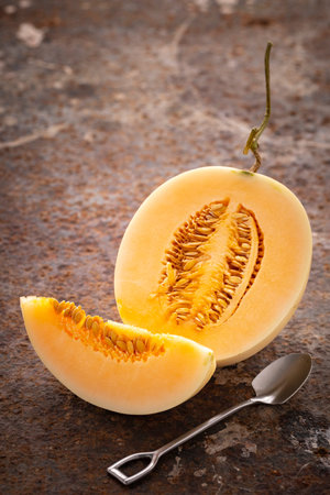 sliced yellow cantaloupe melon with dessert spoon on rusty texture backgroundの写真素材