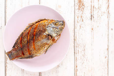 tasty large fried nile tilapia fish in ceramic plate on white wooden texture background with copy space for text, top view, flat lay, light and airy food photographyの写真素材