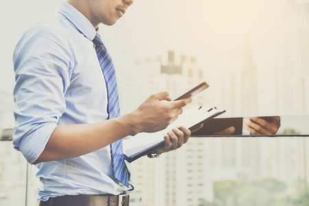 An Asian businessman is using a smartphone to do business with a file in his hand.