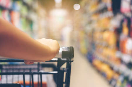 Asian woman's hand with supermarket, trolley and many objects that are blurred background.の写真素材