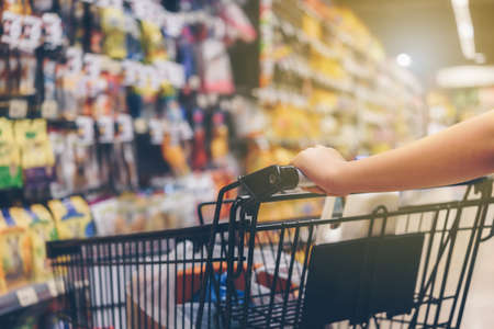 Asian woman's hand with supermarket, trolley and many objects that are blurred background.の写真素材