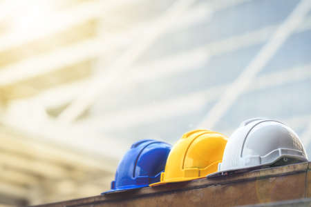 white, yellow and blue hard safety helmet hat for safety project of workman as engineer or worker, on concrete floor on city.の写真素材