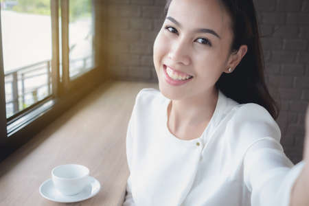 An Asian girl is taking her own picture during a coffee break during the day.の写真素材