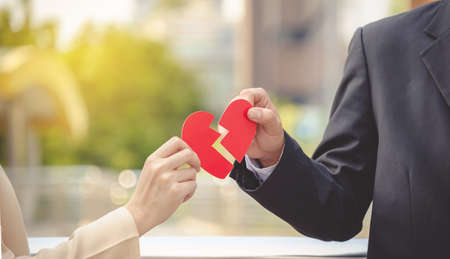 Man and woman pulling a red paper heart apart. The concept of unrequited love. Broken heart.の写真素材