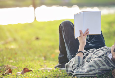 An Asian man is relaxing and reading in the park with evening light.