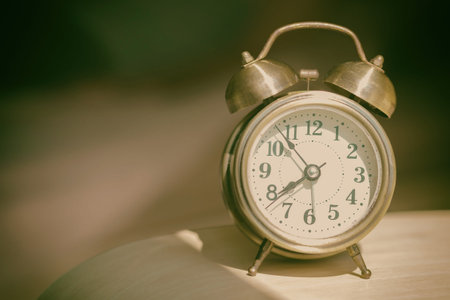 The old alarm clock was set on a wooden desk and there was a man who was blurred as the background.