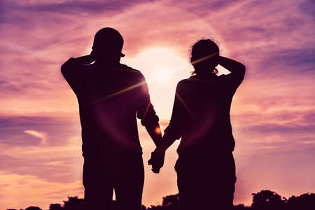 The silhouette of the couple is holding hands and looking at the colorful sunset together.の写真素材