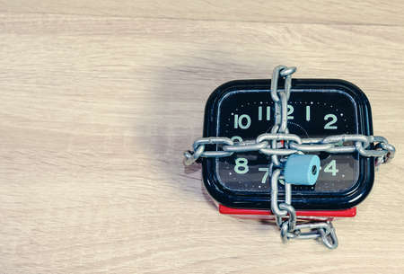 Stopping the time.Old red and black clock with a chain and lock,on wooden floor background.の写真素材