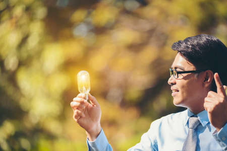 An Asian business man holding a light bulb with a garden blurred in the background.Concept Ideas Idea.の写真素材