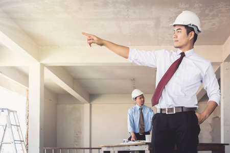 Architects who are standing are pointing their hands at building confidence. There is a background worker blurry.の写真素材