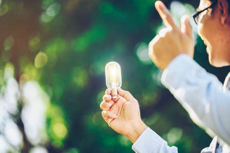 An Asian business man holding a light bulb with a garden blurred in the background.Concept Ideas Idea.の写真素材