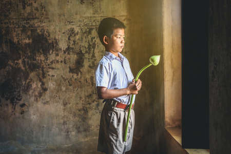A boy is holding a lotus flower for a Buddhist ceremony.の写真素材