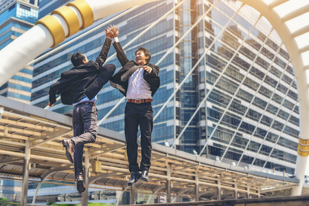 Two Asian businessmen are delighted and jumping, touching each other's hand with success.Concept success in Business.の写真素材