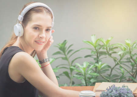 Beautiful women are listening to music with white headphones relaxing and happy in the garden amid green bushes.の写真素材